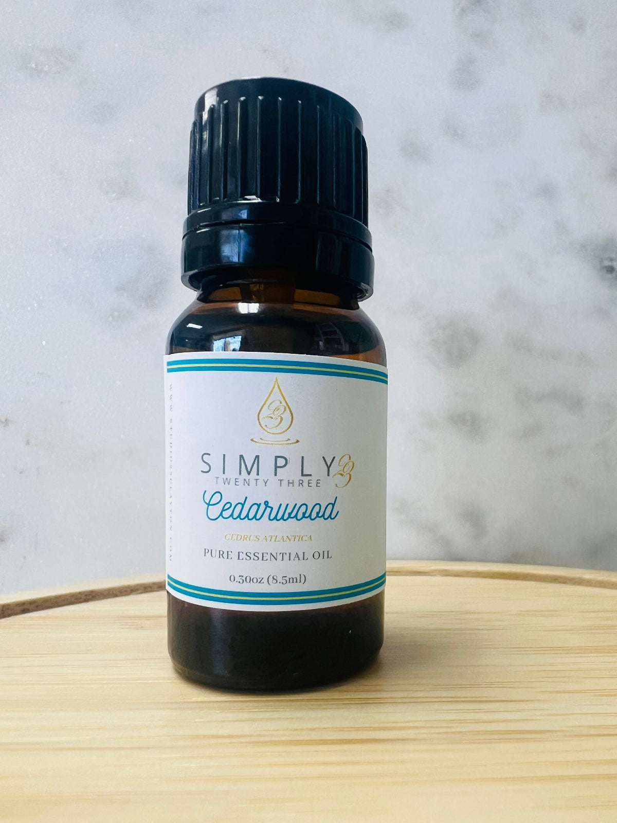 Bottle of Simply 23 Cedarwood essential oil on a wooden surface with a marble background